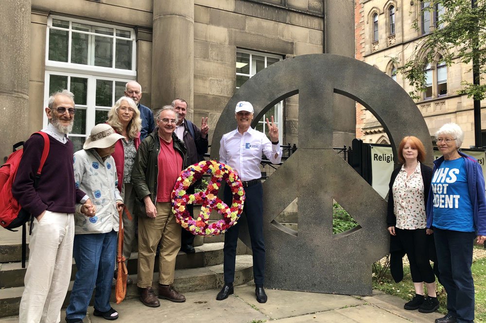 Bernard Weber, Founder of New7Wonders, celebrating the Campaign for Nuclear Disarmament (CND) symbol of peace, while presenting a flower version of the symbol to CND and the Quakers Elders at the Manchester Friends Meeting House.